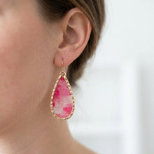 Teardrop-shaped pink earrings with gold frame worn by a person