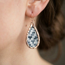 Teardrop-shaped earring with woven design worn by a person