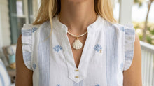 Person wearing a white blouse with blue patterns and a necklace, standing outdoors.