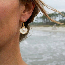 Close-up of a person wearing gold earrings with pearls, with a blurred natural background.
