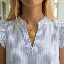 Woman wearing a gold shell pendant necklace with a striped shirt.
