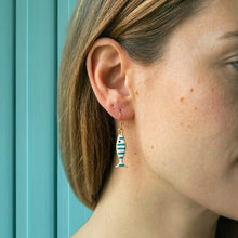 Close-up of a person wearing a fish-shaped earring with a turquoise background
