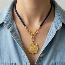 Gold necklace with a pendant worn by a person wearing a denim shirt.