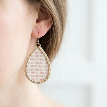 Teardrop-shaped earrings with a textured design worn by a person.