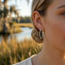 Close-up of a person wearing hoop earrings with a blurred natural background