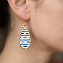 Teardrop-shaped earring with blue and white pattern worn by a person.