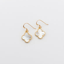 Gold earrings with clover-shaped white stones on a light gray background