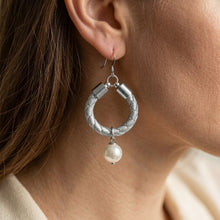 Silver hoop earring with a pearl pendant worn by a person.