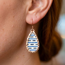 Teardrop-shaped earring with blue and white pattern worn by a person.