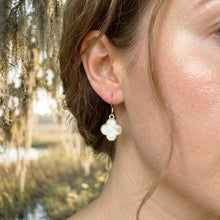 Close-up of a person wearing a clover-shaped earring with a natural background