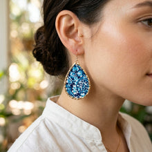 Close-up of a woman wearing blue teardrop earrings with a blurred outdoor background