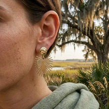 Close-up of a person wearing a gold earring with a natural landscape in the background