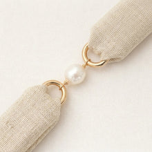 Beige ribbon with gold rings and a pearl on a light beige background