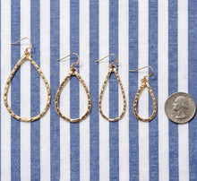 Four pairs of gold hoop earrings on a blue and white striped background with a quarter for scale.