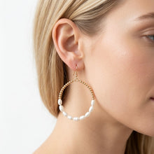 Gold hoop earring with pearl beads worn by a person on a light background