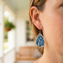 Close-up of a person wearing blue teardrop earrings with a blurred outdoor background