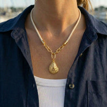 Person wearing a gold necklace with a pendant, dressed in a dark blue shirt and white pants.