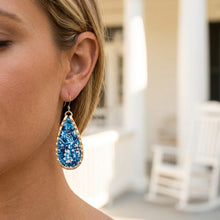 Close-up of a woman wearing blue teardrop earrings with a blurred indoor background