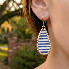 Teardrop-shaped earring with blue and white striped pattern worn by a person outdoors.