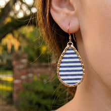 Teardrop-shaped earring with blue and white striped design worn by a person outdoors.