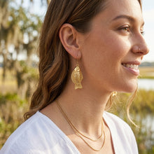 Woman wearing gold earrings and necklace with a blurred natural background