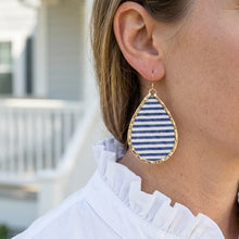 Teardrop-shaped earring with blue and white stripes worn by a person.
