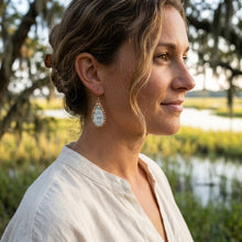 Woman wearing earrings with a natural background of trees and water