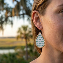 Close-up of a person wearing a gold earring with text, outdoors.