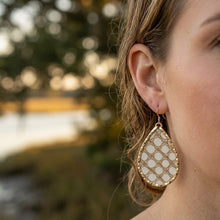 Close-up of a woman wearing gold and white patterned earrings with a blurred natural background.