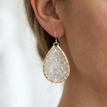 Teardrop-shaped earring worn by a person with a plain background