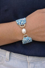 Bracelet with blue ceramic pieces and a pearl on a wrist against a dark shirt.