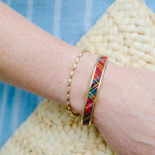 Gold bracelet with a colorful pattern worn on a wrist against a blue and beige background