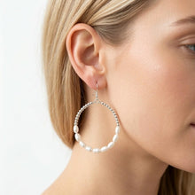 Close-up of a woman wearing pearl hoop earrings with a plain background