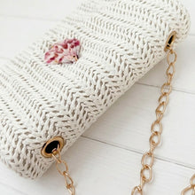 White textured clutch bag with a floral detail and gold chain strap on a light wooden surface.