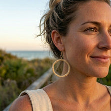 Woman wearing large hoop earrings with a beach background