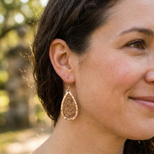 Close-up of a woman wearing a gold teardrop earring with a blurred natural background