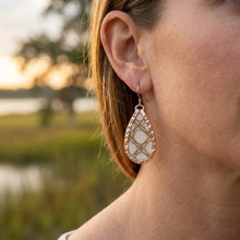 Close-up of a person wearing a teardrop-shaped earring with a blurred natural background