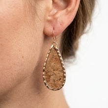 Teardrop-shaped cork earring worn by a person on a blurred background