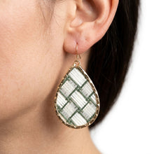 Teardrop-shaped earring with green and white pattern worn by a person