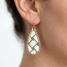 Teardrop-shaped earring with green and white pattern worn by a person