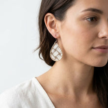 Close-up of a woman wearing a teardrop-shaped earring with a white and gold pattern on a light gray background.