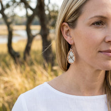 Woman wearing rose gold earrings with a blurred natural background