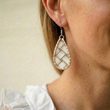 Teardrop-shaped earring worn by a person with a neutral background