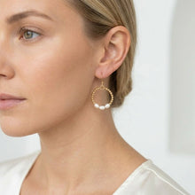 Close-up of a woman wearing gold hoop earrings with pearls on a white background