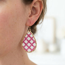 Teardrop-shaped earring with pink and white pattern worn by a person.