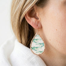 Teardrop-shaped earring with green and white pattern worn by a person.