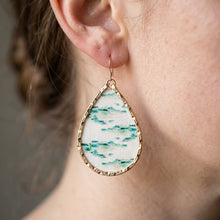Teardrop-shaped earring with gold frame and green and white pattern worn by a person.