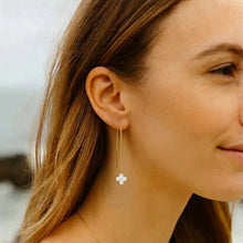 Close-up of a woman wearing gold earrings with a cross pendant.