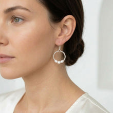 Close-up of a woman wearing silver hoop earrings with pearls on a white background
