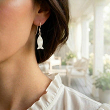 Close-up of a person wearing fish-shaped earrings with a blurred indoor background.